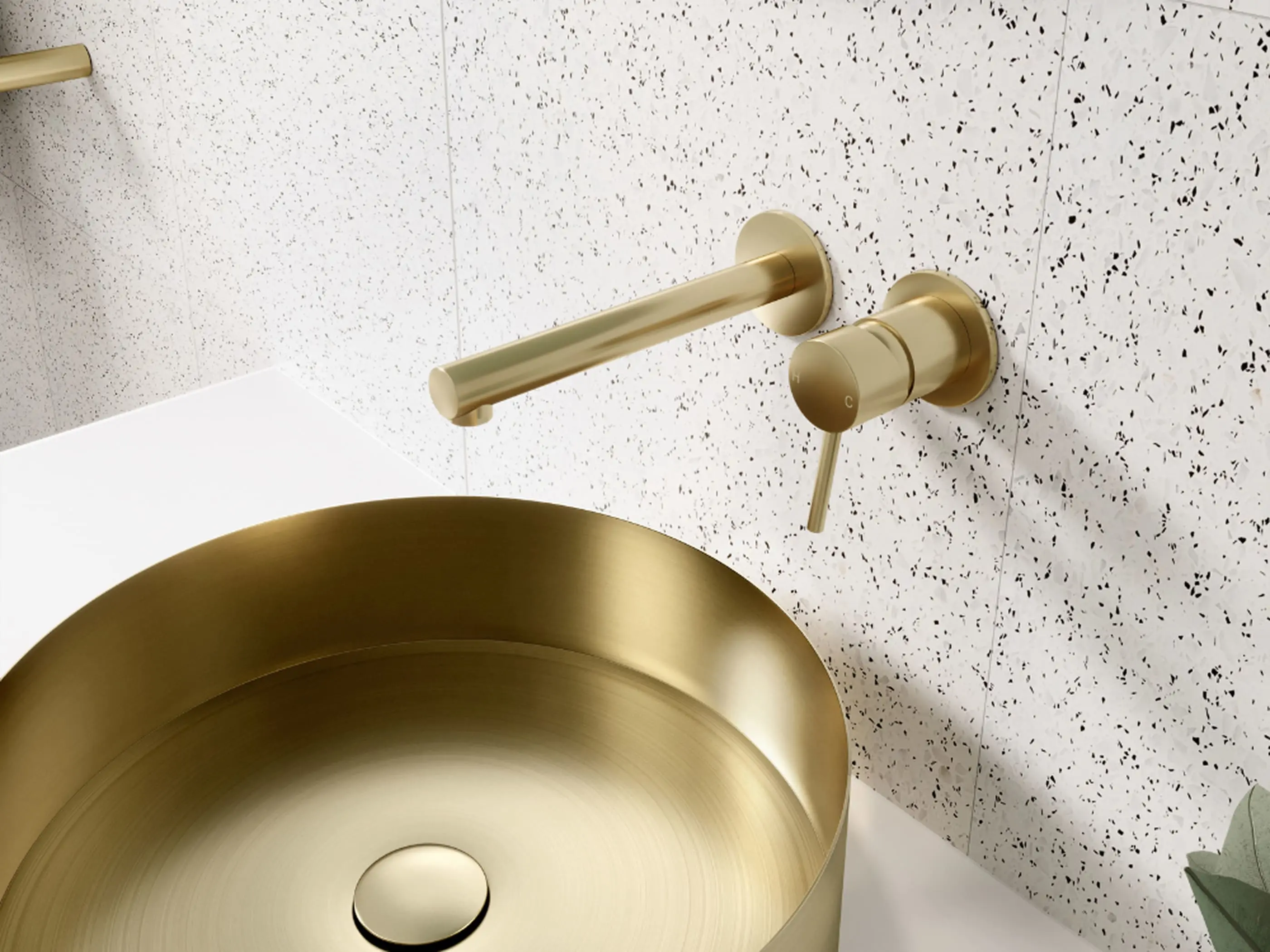 Gold bathroom fixtures including wall-mounted faucet and circular sink basin against white speckled tile wall.