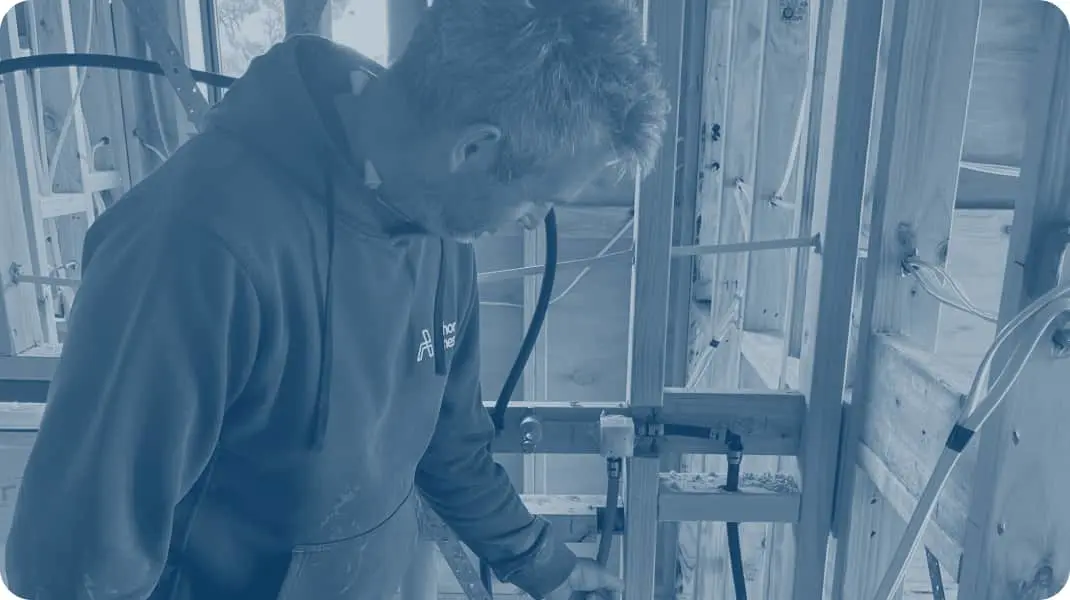 Construction worker in hoodie examining wooden framing inside unfinished building with exposed wiring.