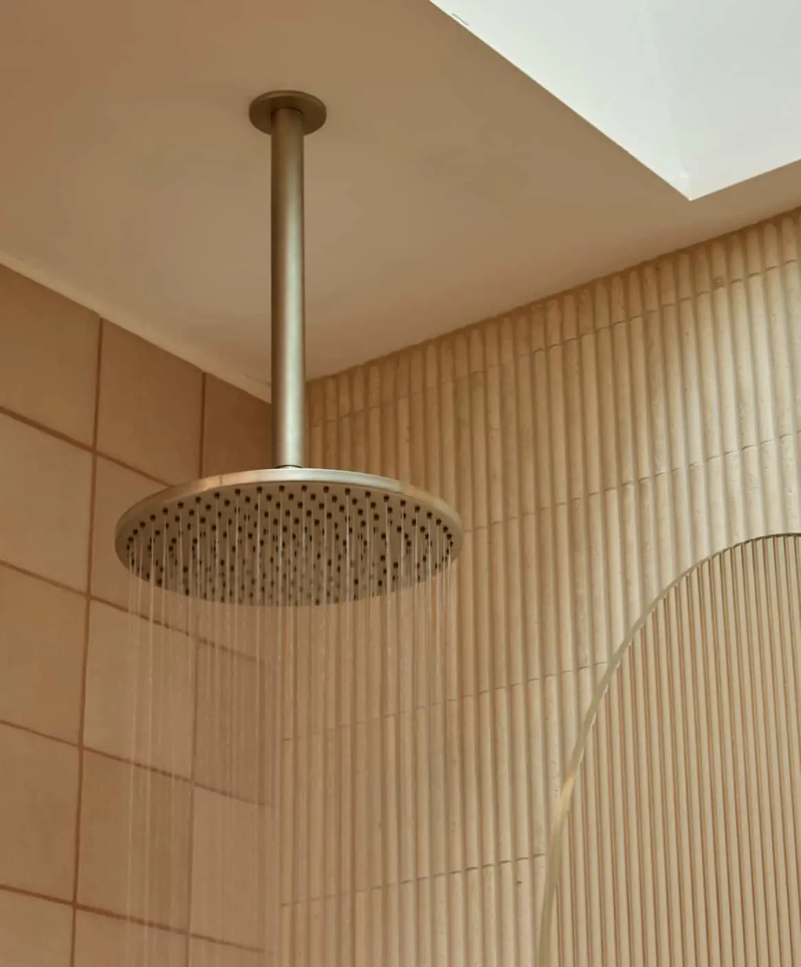Modern bathroom with ceiling-mounted rainfall shower head and curved-edge shower screen.