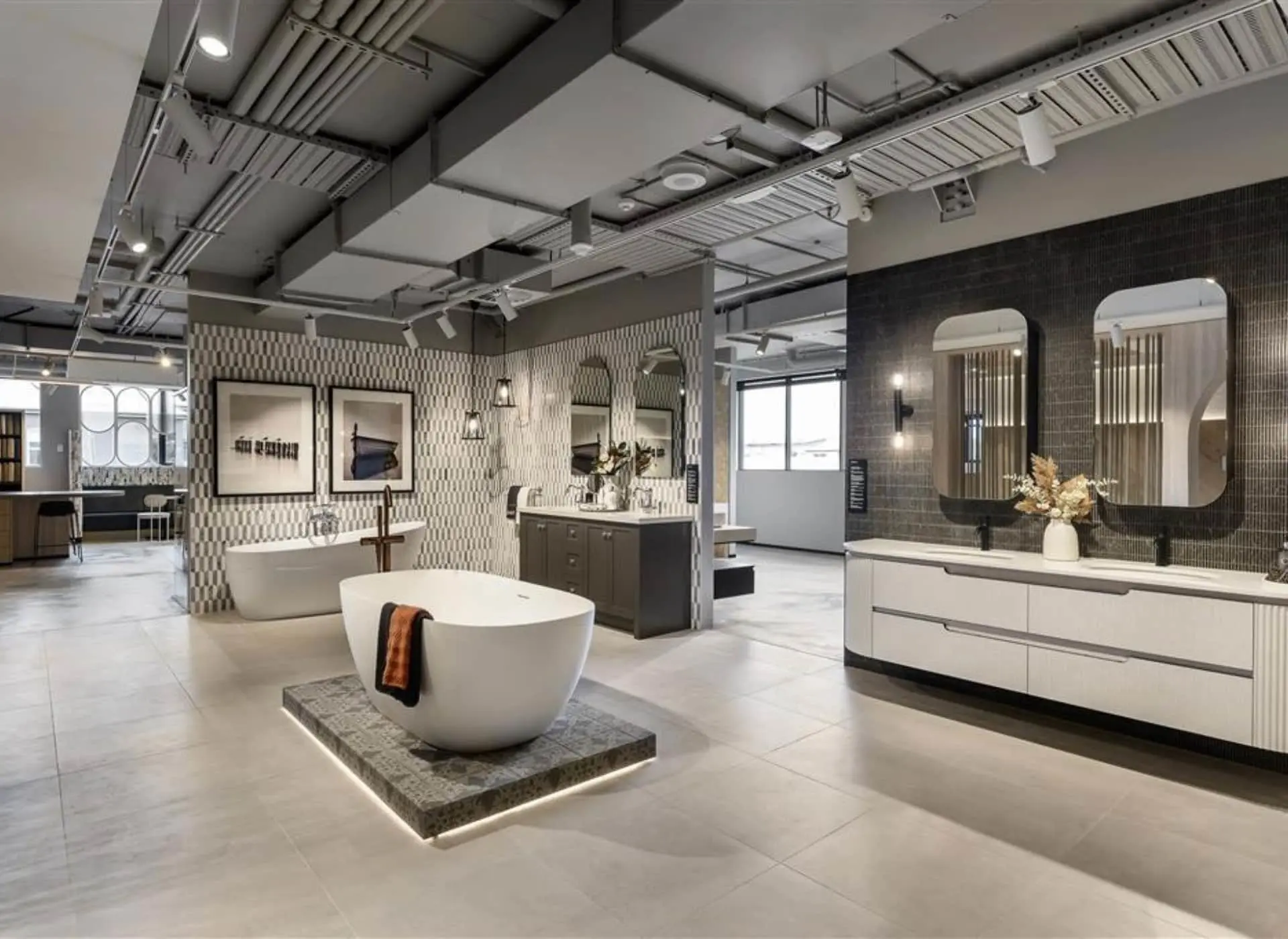 Modern bathroom showroom with freestanding white tubs, patterned walls, vanities, and mirrors in industrial-style space.