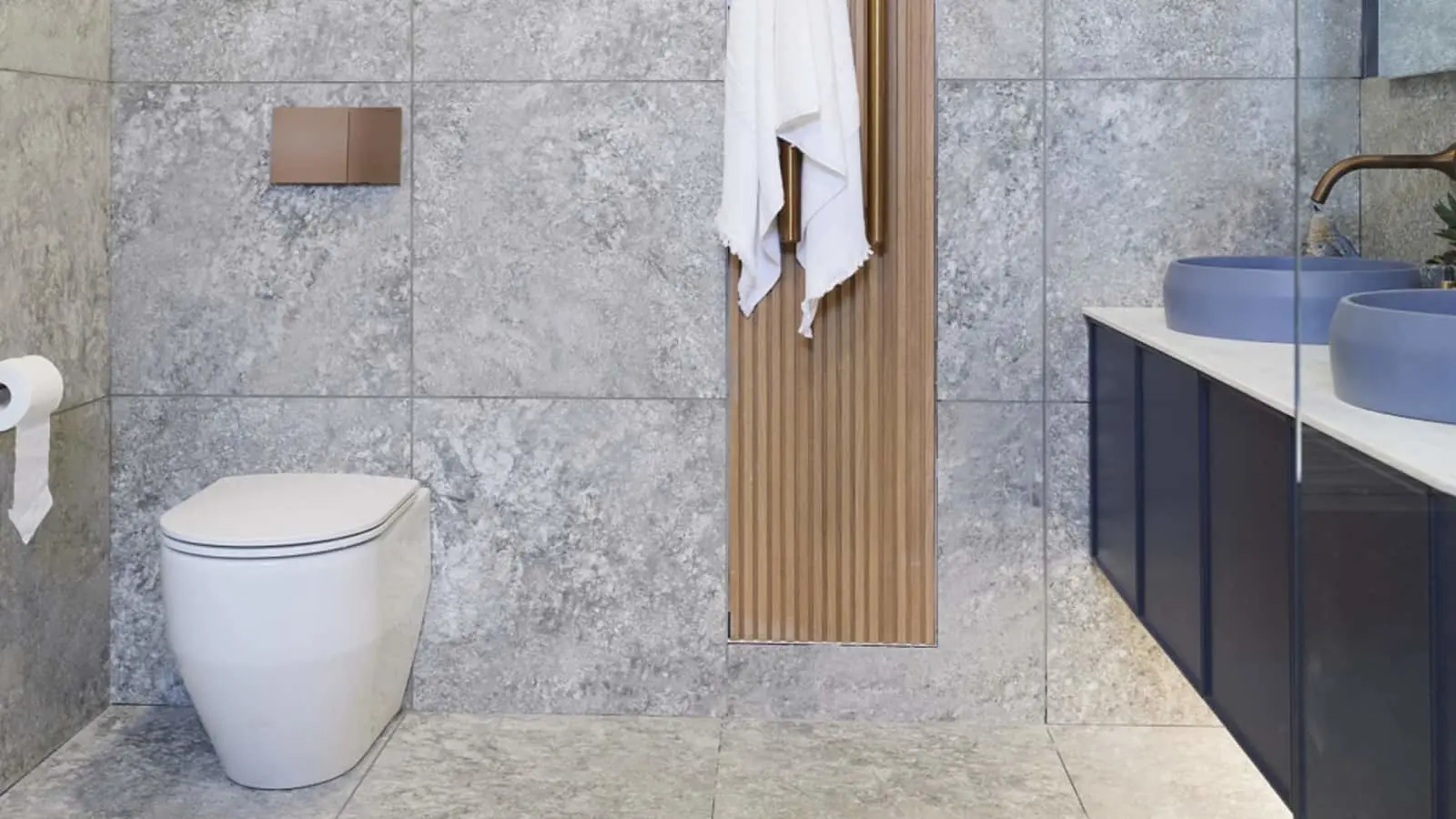 Modern bathroom with gray marble tiles, white toilet, wooden accent panel, and blue vessel sink on dark vanity.