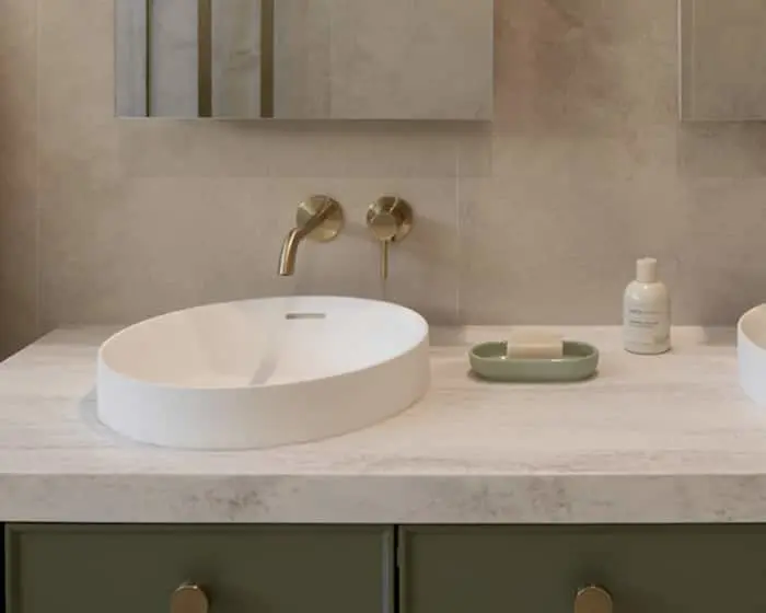 Modern bathroom with oval white sink, brass wall-mounted faucet, and marble countertop with minimal toiletries.