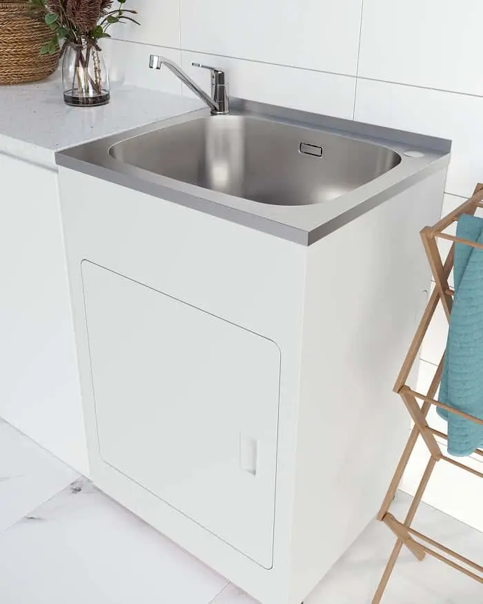 Modern stainless steel laundry sink with chrome faucet in white cabinet, wooden drying rack with blue towel nearby.
