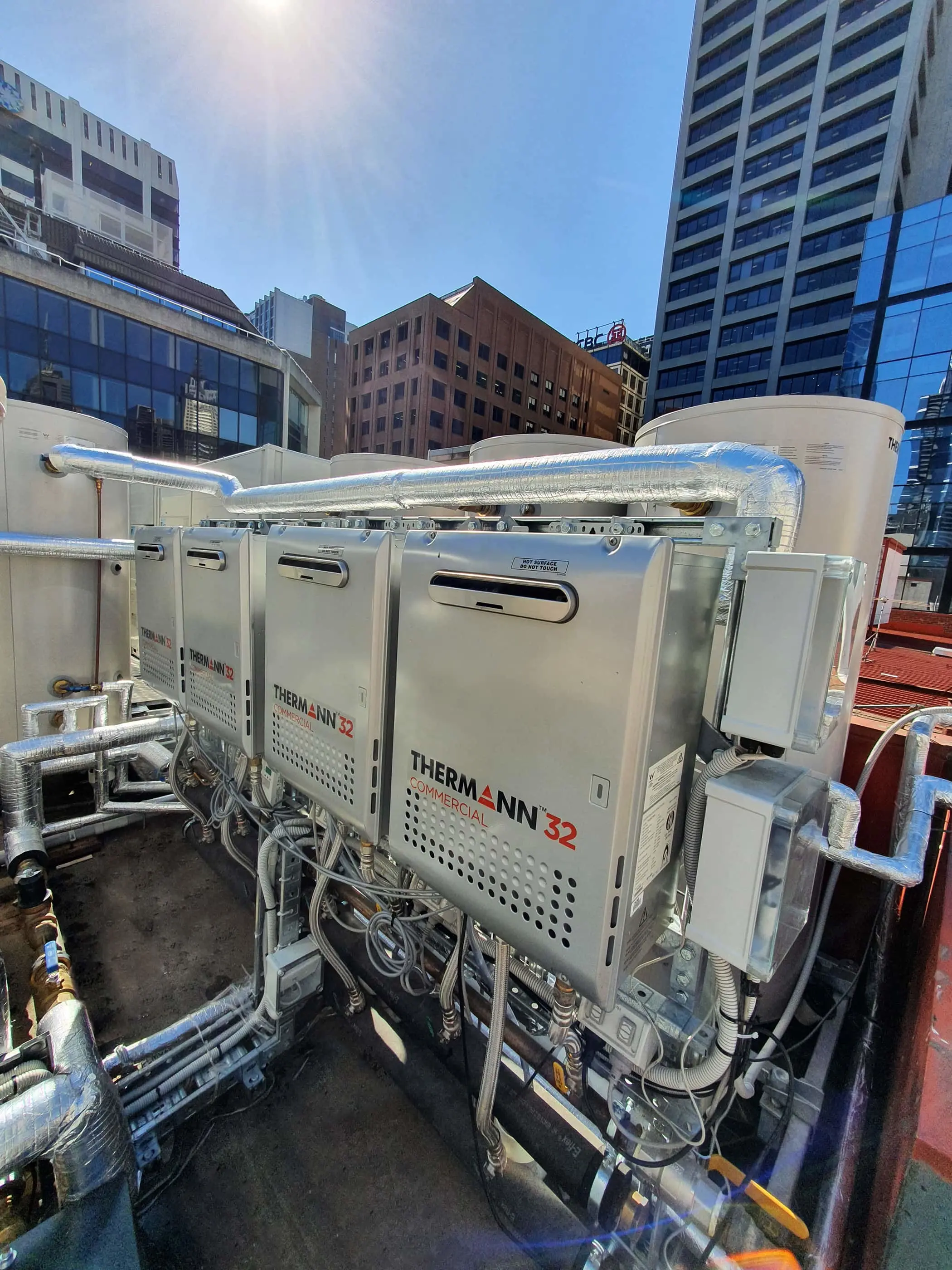 Thermann commercial water heaters installed on a rooftop with city buildings in the background under blue sky.