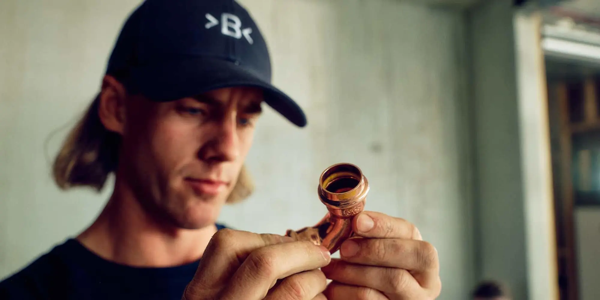 Person wearing a black cap holding a small copper pipe in their hands indoors.