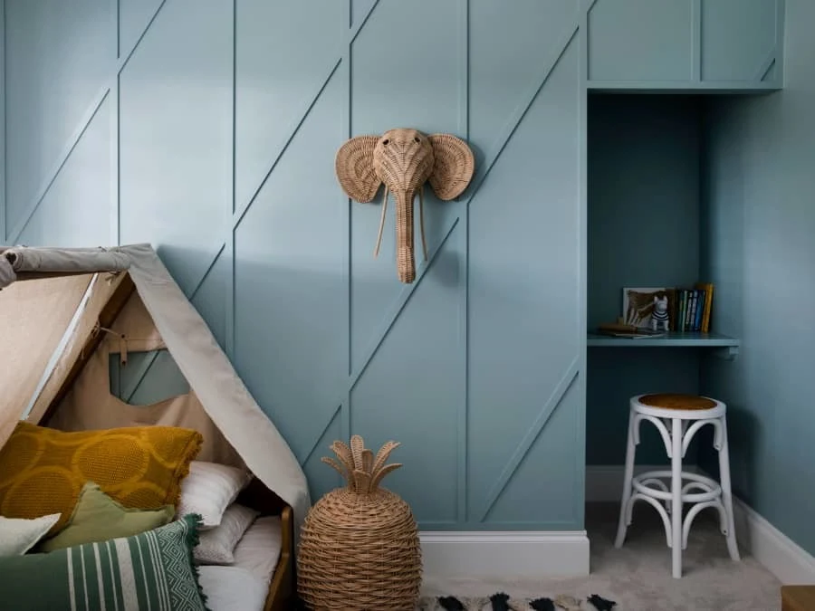 Child's room with teal walls, canvas tent, wicker elephant head decoration, pineapple basket, and small reading nook.