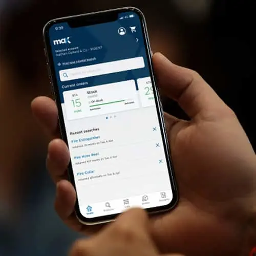 Hand holding smartphone displaying the maX app interface with current orders and recent searches.