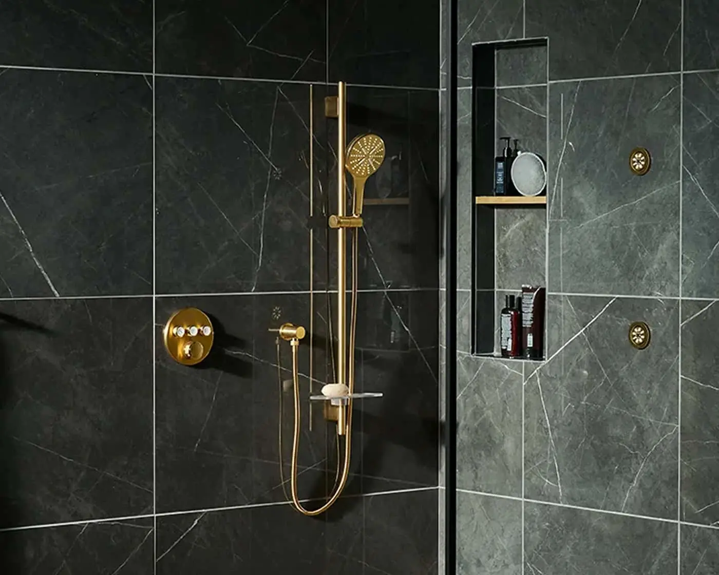 Modern bathroom with dark marble tiles, gold shower fixtures, and built-in wall niche for toiletries.