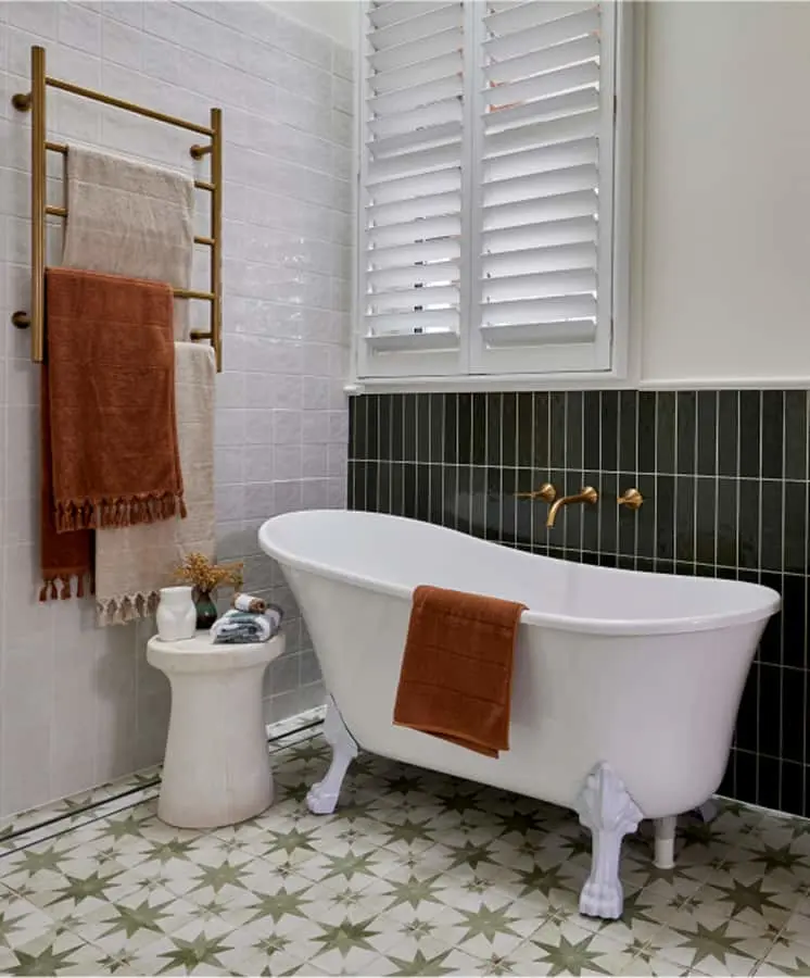 Modern bathroom with white clawfoot tub, green tile accent wall, brass towel rack, and patterned floor tiles.