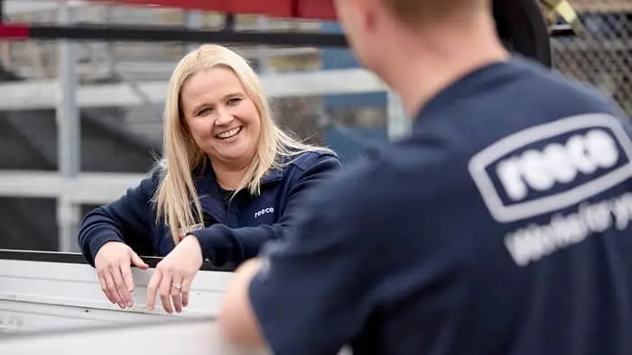 Two colleagues in navy blue uniforms having a friendly conversation at an industrial worksite.