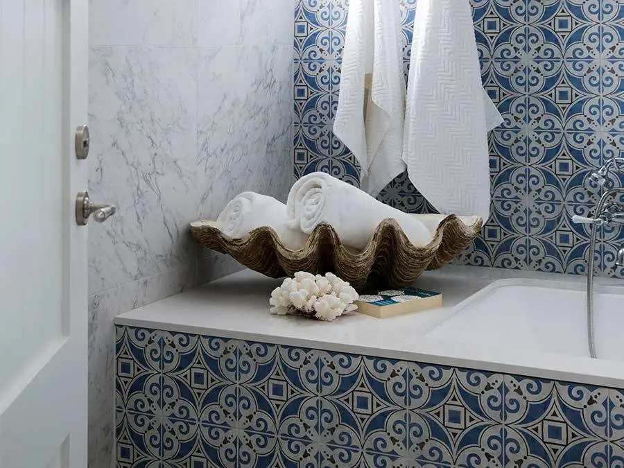 Bathroom with blue patterned tiles, marble wall, large shell holding white towels, and coral decoration on bathtub edge.