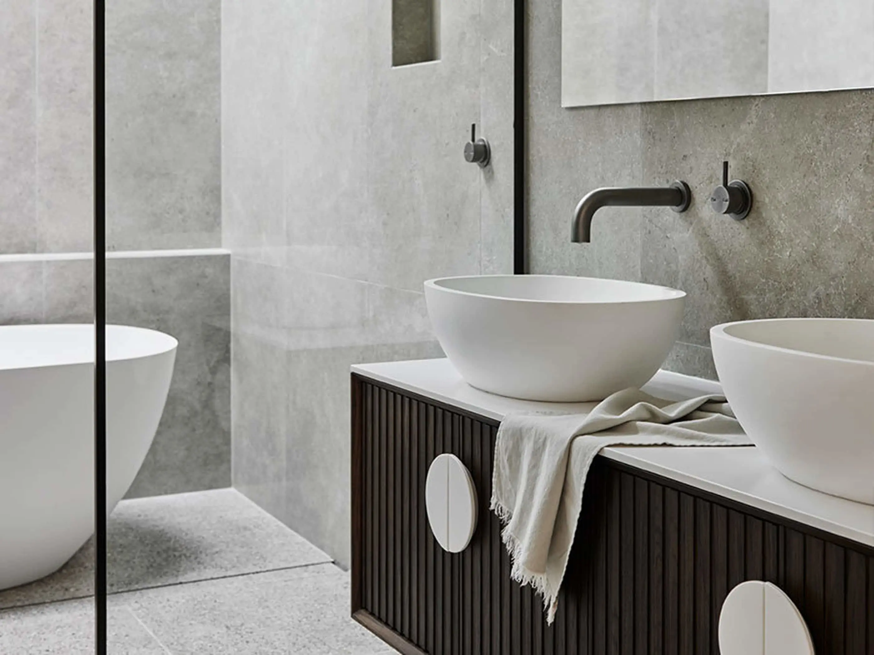 Modern bathroom with white vessel sinks on dark wood vanity, concrete walls, and wall-mounted faucets.