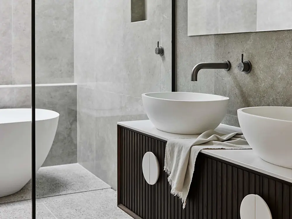 Modern bathroom with white vessel sinks on dark wood vanity, concrete walls, and wall-mounted faucets.