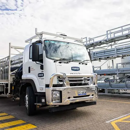 White Reece truck with roof rack parked in front of metal scaffolding under cloudy sky.