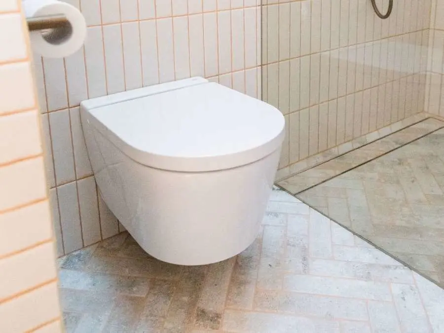 Modern wall-mounted white toilet in bathroom with beige tiled walls and herringbone pattern floor tiles.
