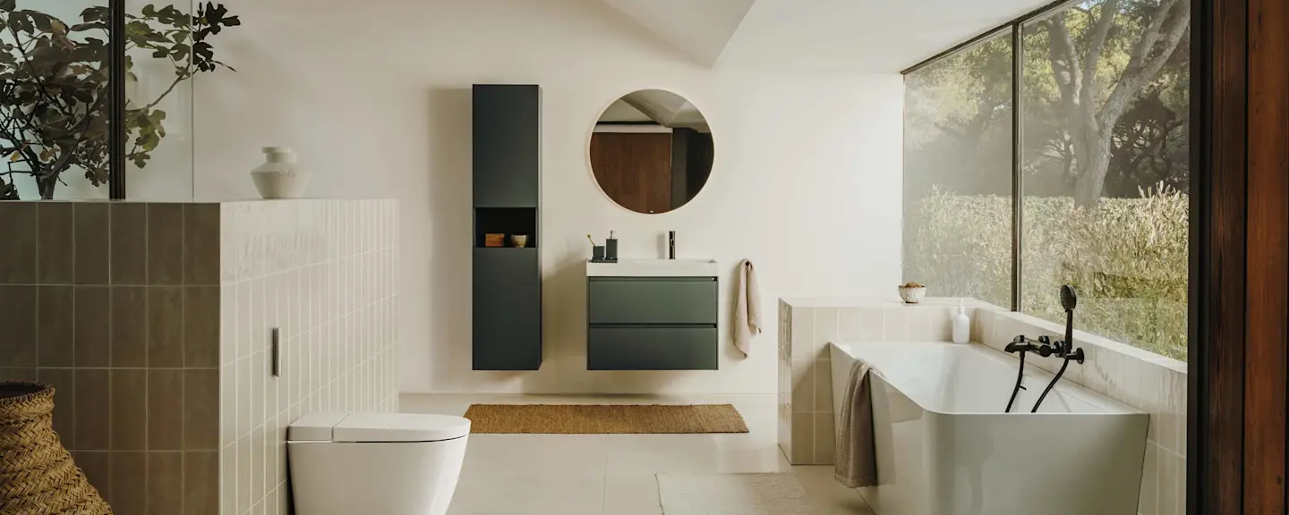 Modern bathroom with white freestanding tub, round mirror, floating vanity, and large window overlooking trees.