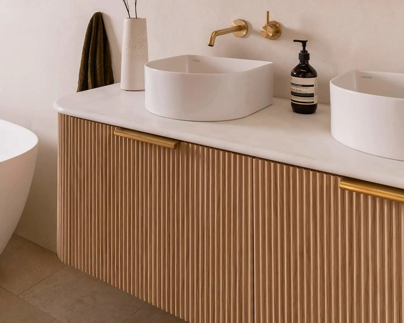 Modern bathroom with white vessel sinks on wooden vanity, brass fixtures, and minimalist decor.
