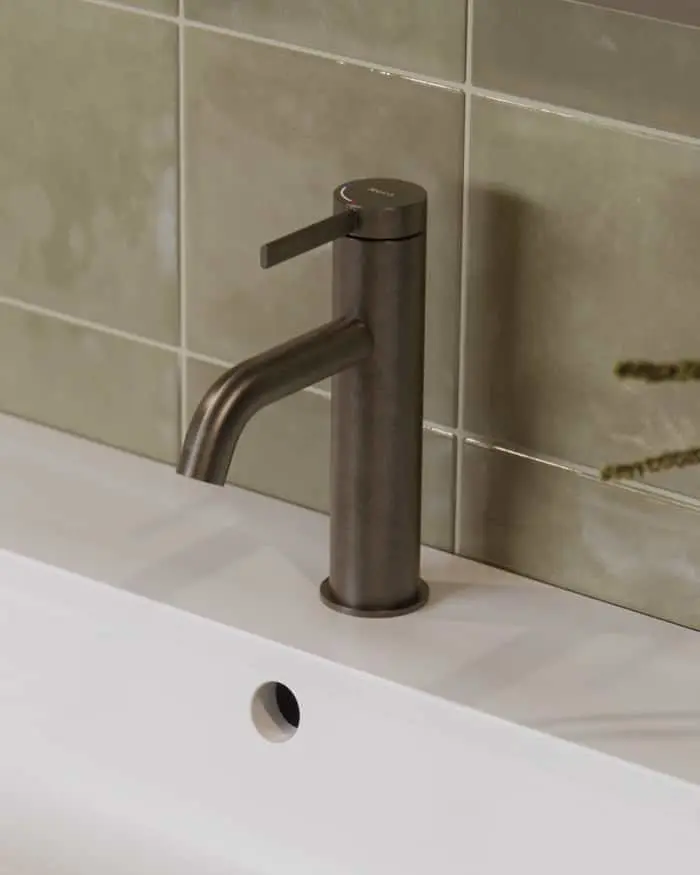 Bronze bathroom faucet on white sink with beige tile wall background