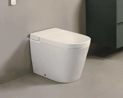 White modern toilet with closed lid in a bathroom corner with gray walls and beige floor.