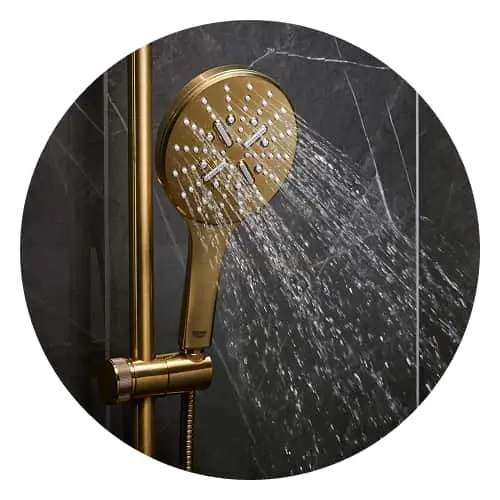 Gold handheld shower head spraying water against dark marble bathroom wall