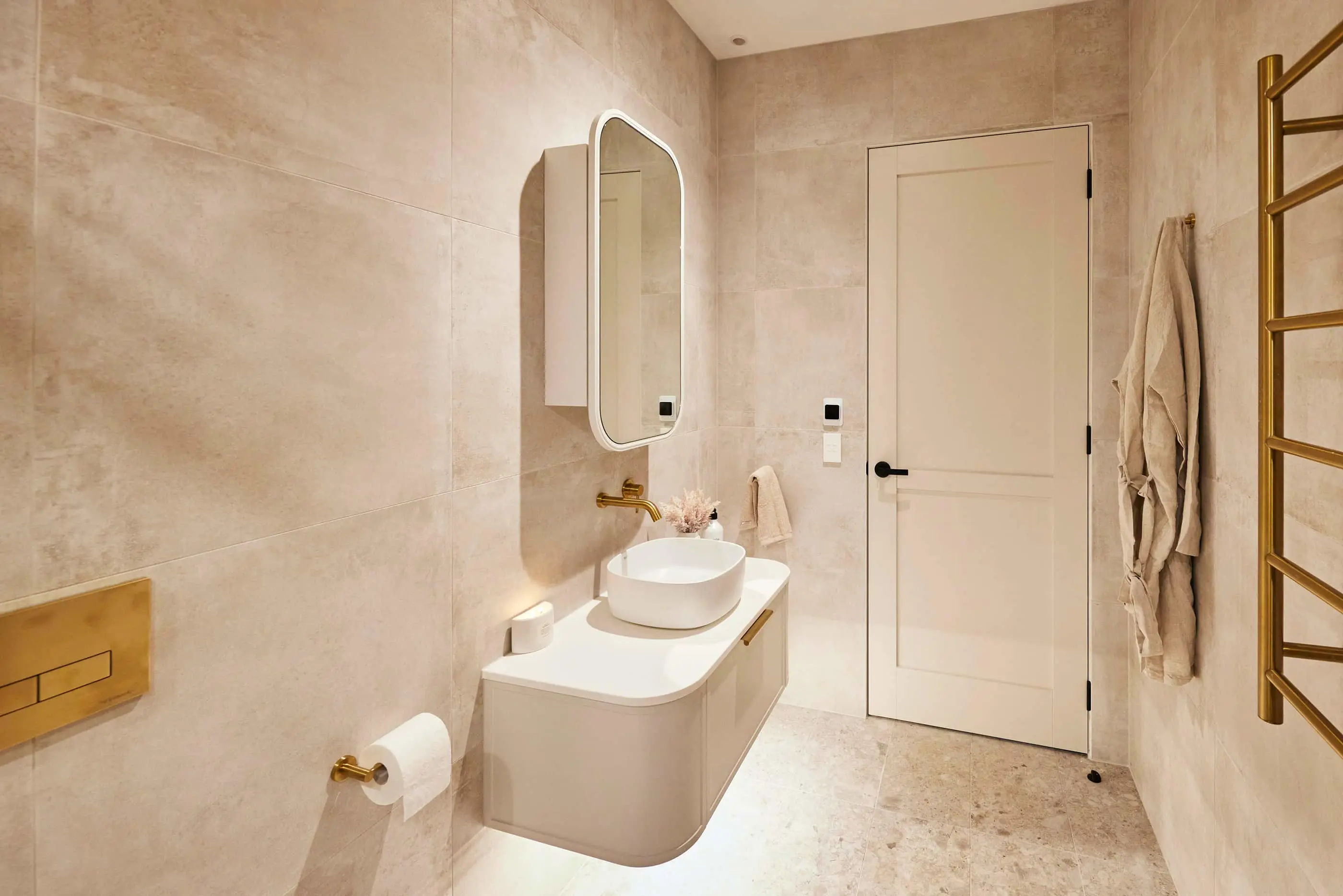 Modern bathroom with beige walls, white vanity with vessel sink, gold fixtures, and a towel warming rack.