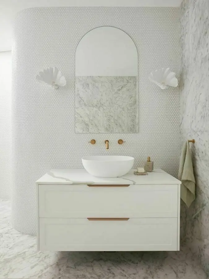 Elegant white bathroom with marble accents, arched mirror, vessel sink, and brass fixtures on a floating vanity cabinet.