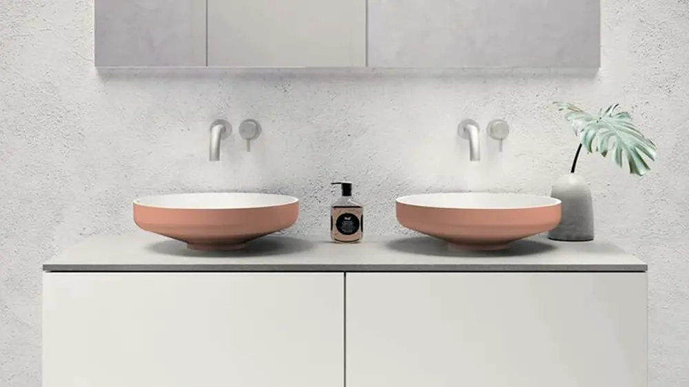 Modern bathroom with two pink vessel sinks on white vanity, wall-mounted faucets, and small plant in vase.