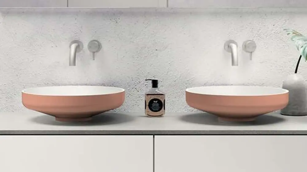 Modern bathroom with two pink vessel sinks on white vanity, wall-mounted faucets, and small plant in vase.