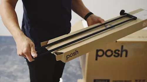 Person in dark clothing holding a black metal rod and cardboard boxes labeled "posh" for assembly or installation.