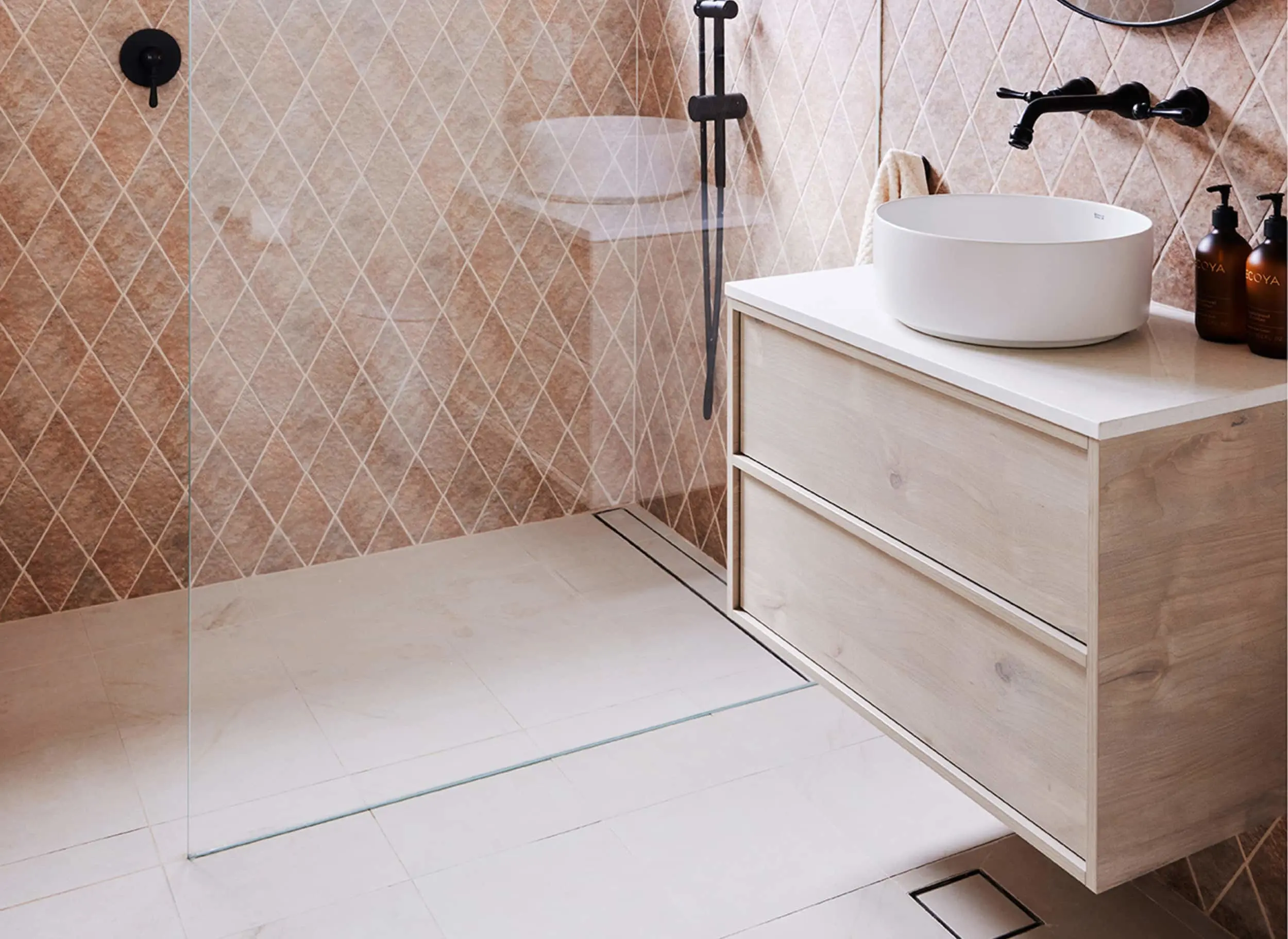 Modern bathroom with terracotta diamond-patterned tiles, white vessel sink on wooden vanity, and black fixtures.