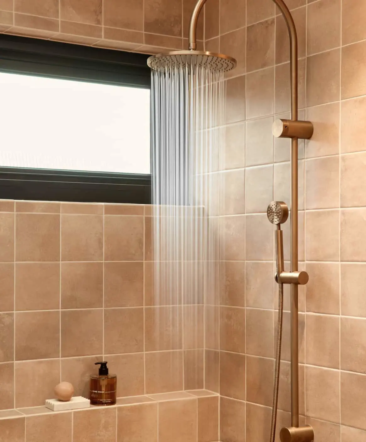 Modern bathroom with brass rainfall shower and beige tiled walls.