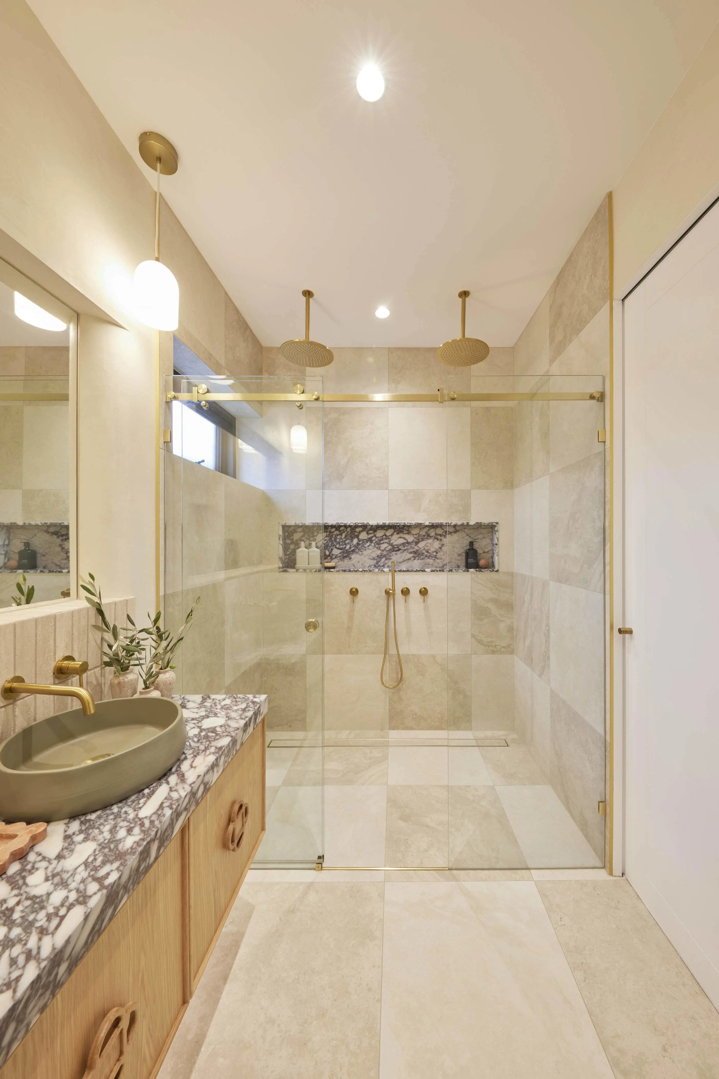 Modern bathroom with glass shower, beige tile walls, marble countertop, green sink, and gold fixtures.