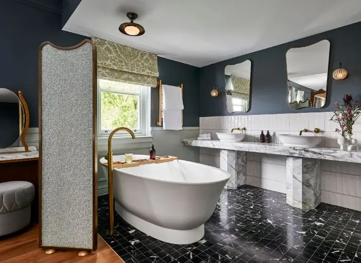 Elegant bathroom with freestanding tub, marble countertops, dark blue walls, and black tile flooring.