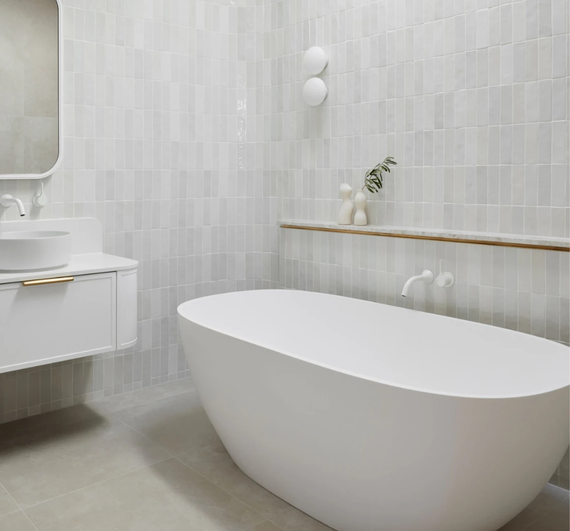 Modern white bathroom with freestanding tub, wall-mounted sink, and light gray tile walls featuring a small shelf with decorative items.