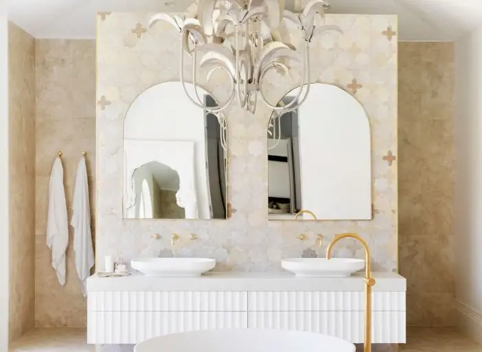 Elegant bathroom with beige walls, white vanity with dual vessel sinks, arched mirrors, and a crystal chandelier.
