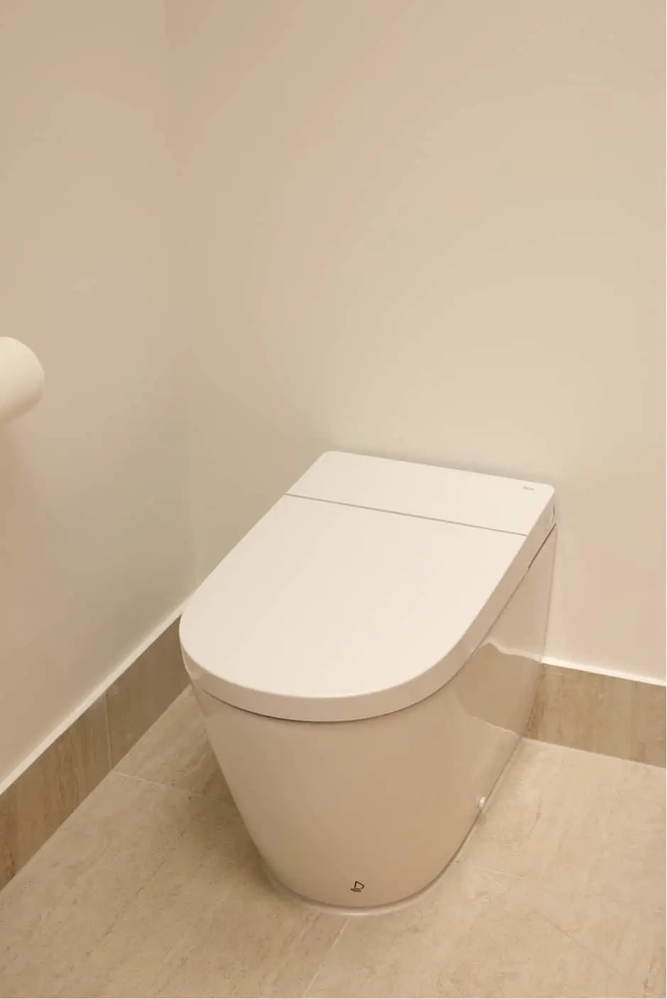 White modern toilet with closed lid in a beige bathroom with tiled floor and walls.