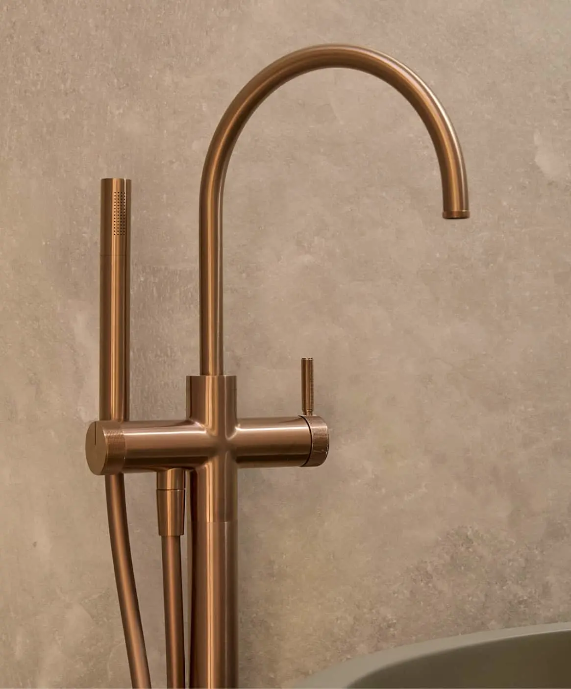 Modern bronze bathroom floor-mounted faucet with high curved spout against a beige stone wall