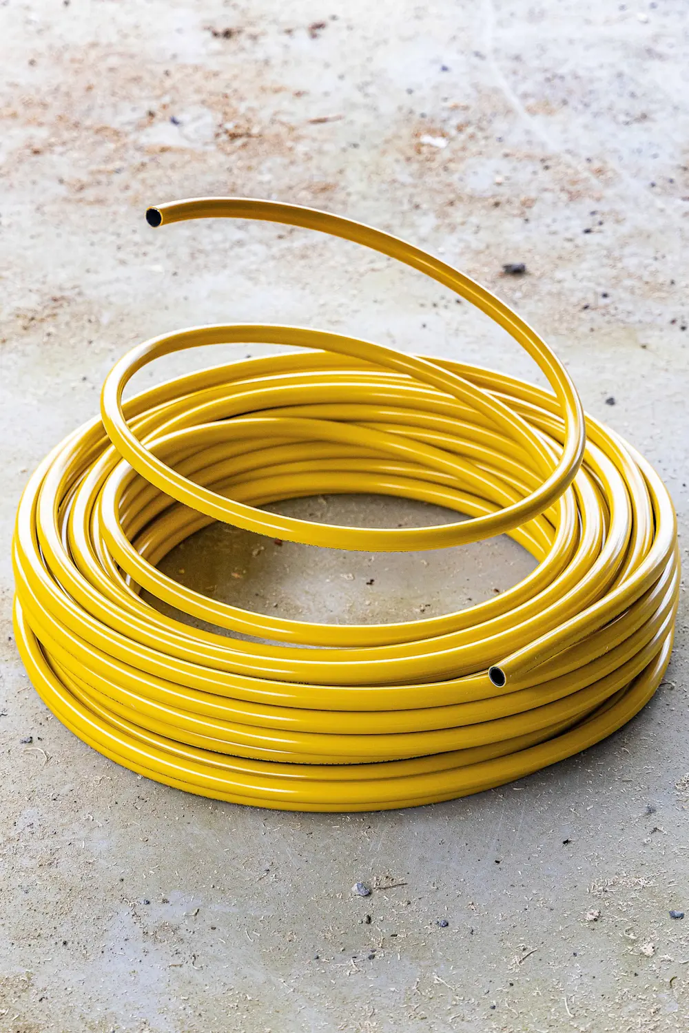 Coiled yellow pipe with one end extended upward, resting on a concrete surface.