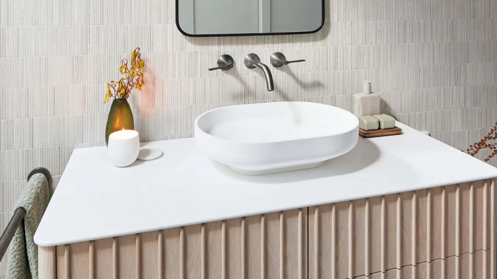 Modern bathroom with white oval sink, wall-mounted faucet, wooden cabinet, and decorative vase with candle.
