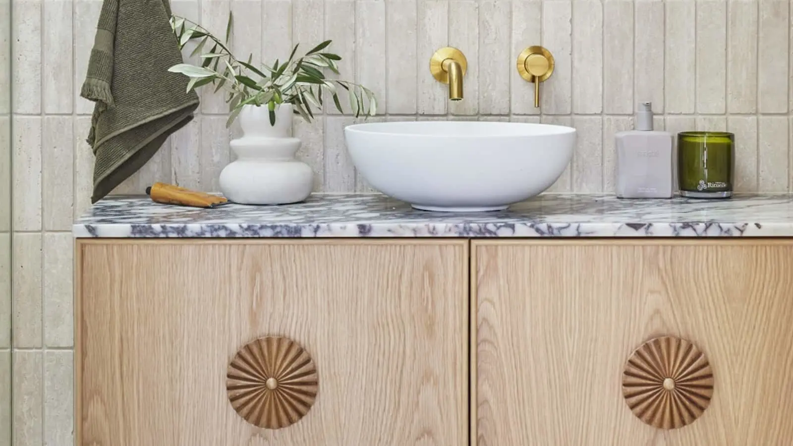 Modern bathroom vanity with white vessel sink, gold fixtures, marble countertop, and wooden cabinets with decorative handles.