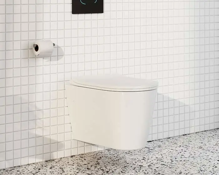 Modern white wall-mounted toilet in a bathroom with white tile walls and speckled terrazzo flooring.