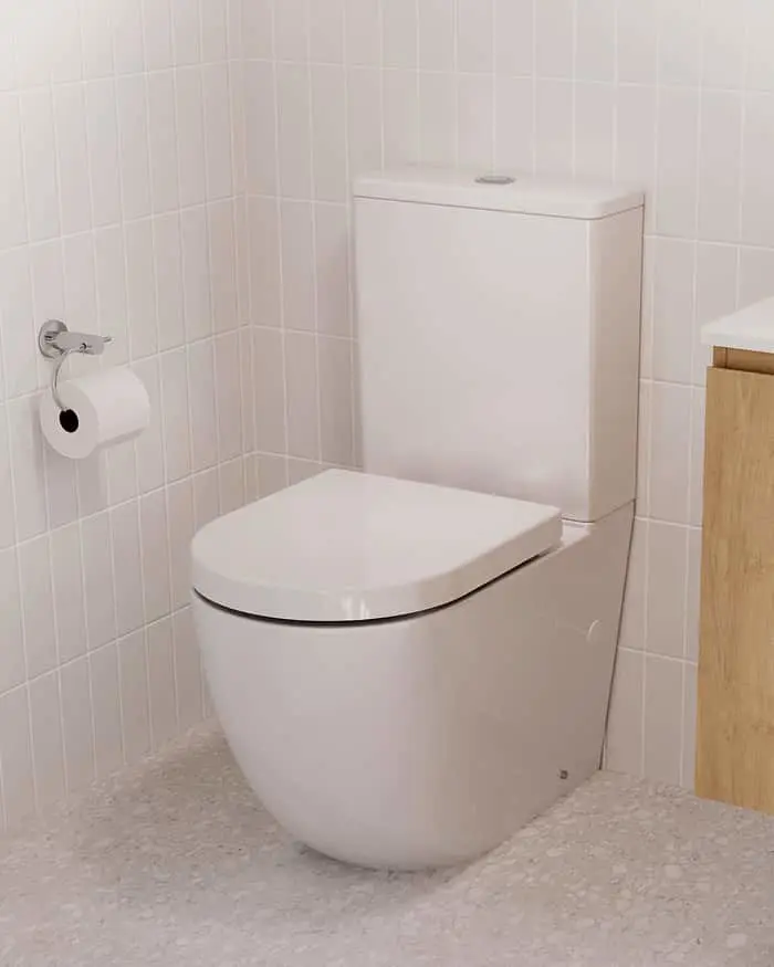 White toilet with closed lid in a bathroom with white tiled walls, toilet paper holder, and wooden cabinet edge visible.
