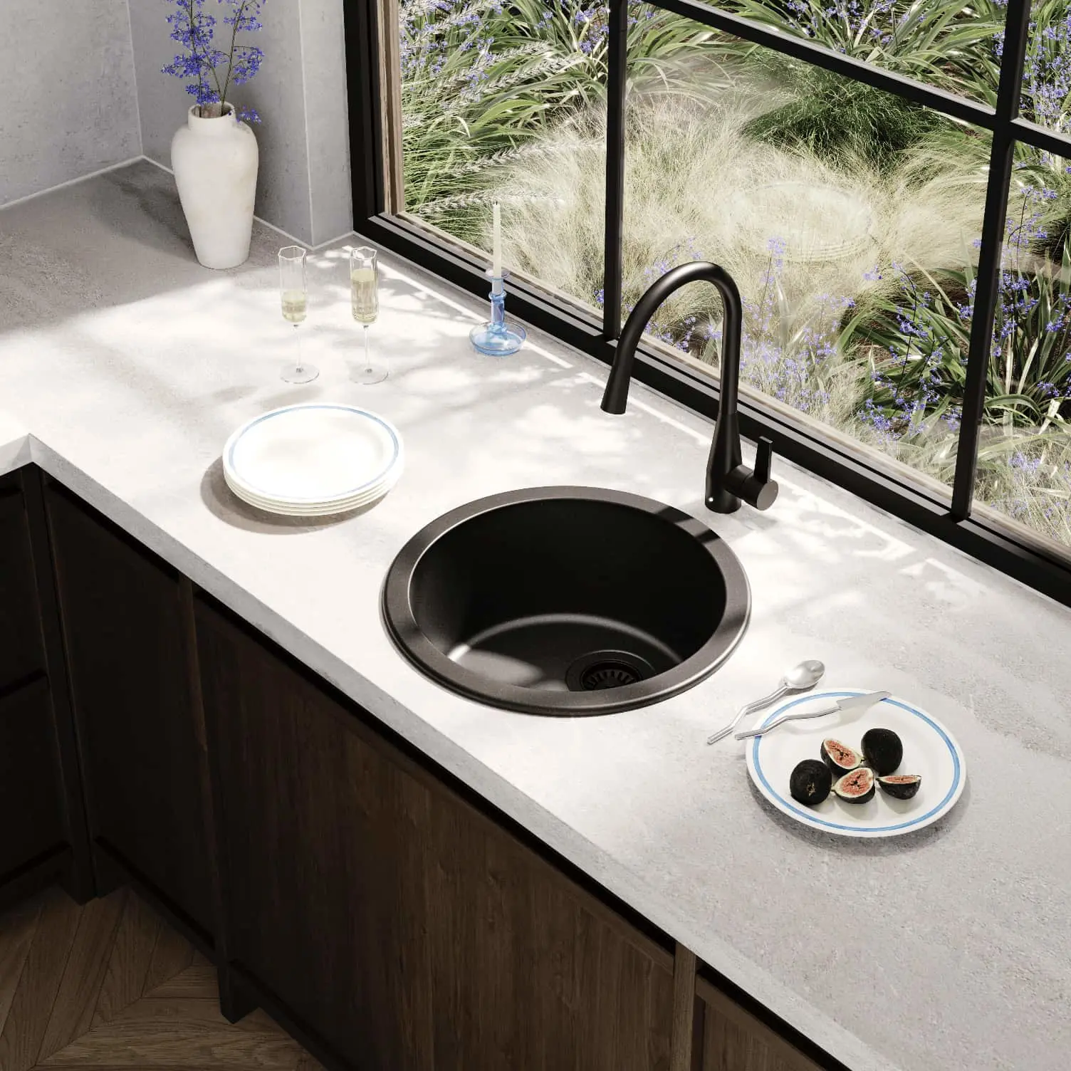 Modern kitchen counter with black round sink, white countertop, and large window overlooking ornamental grasses.