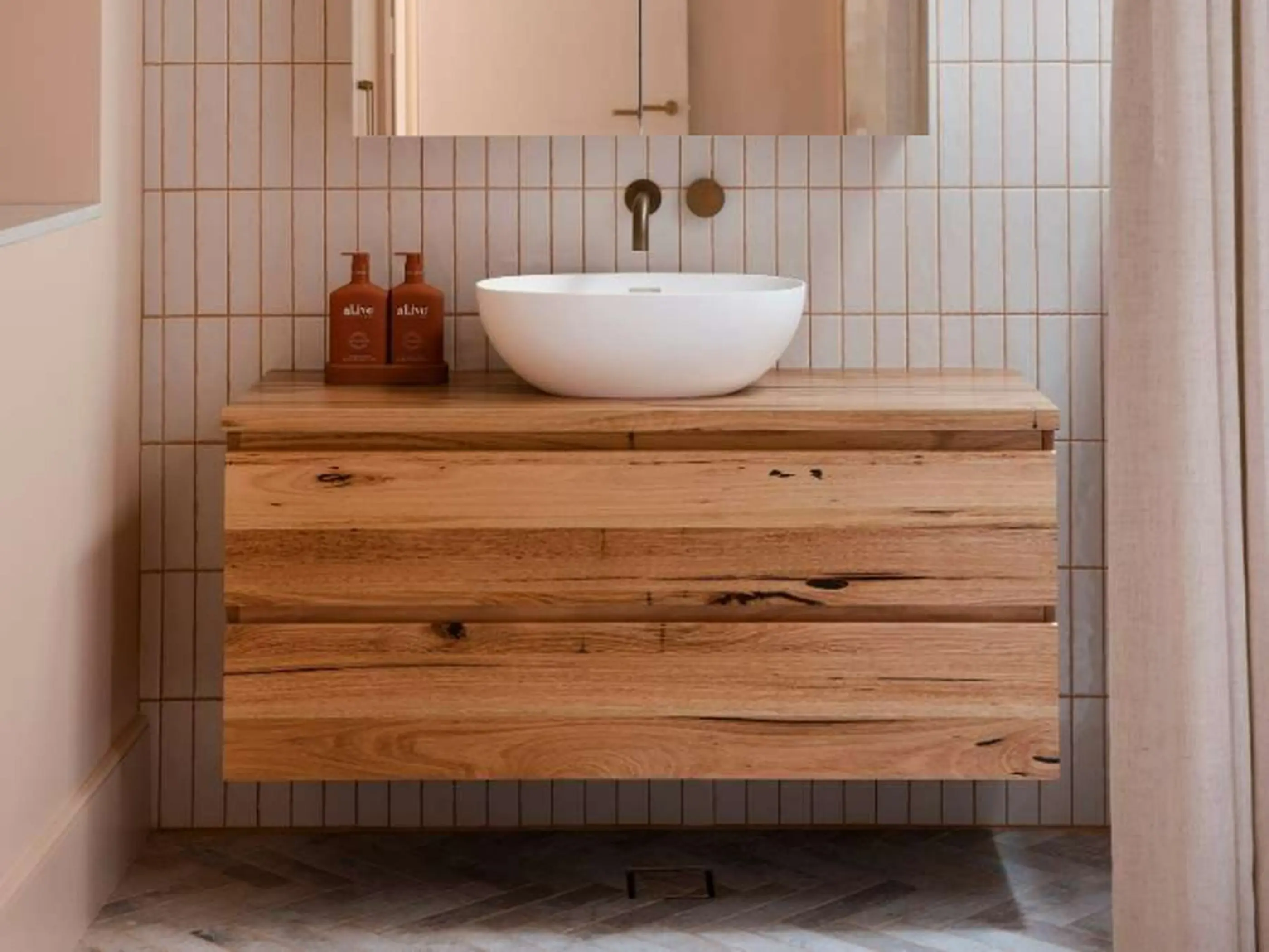 Modern bathroom with white vessel sink on wooden floating vanity, vertical tile backsplash, and brass fixtures.