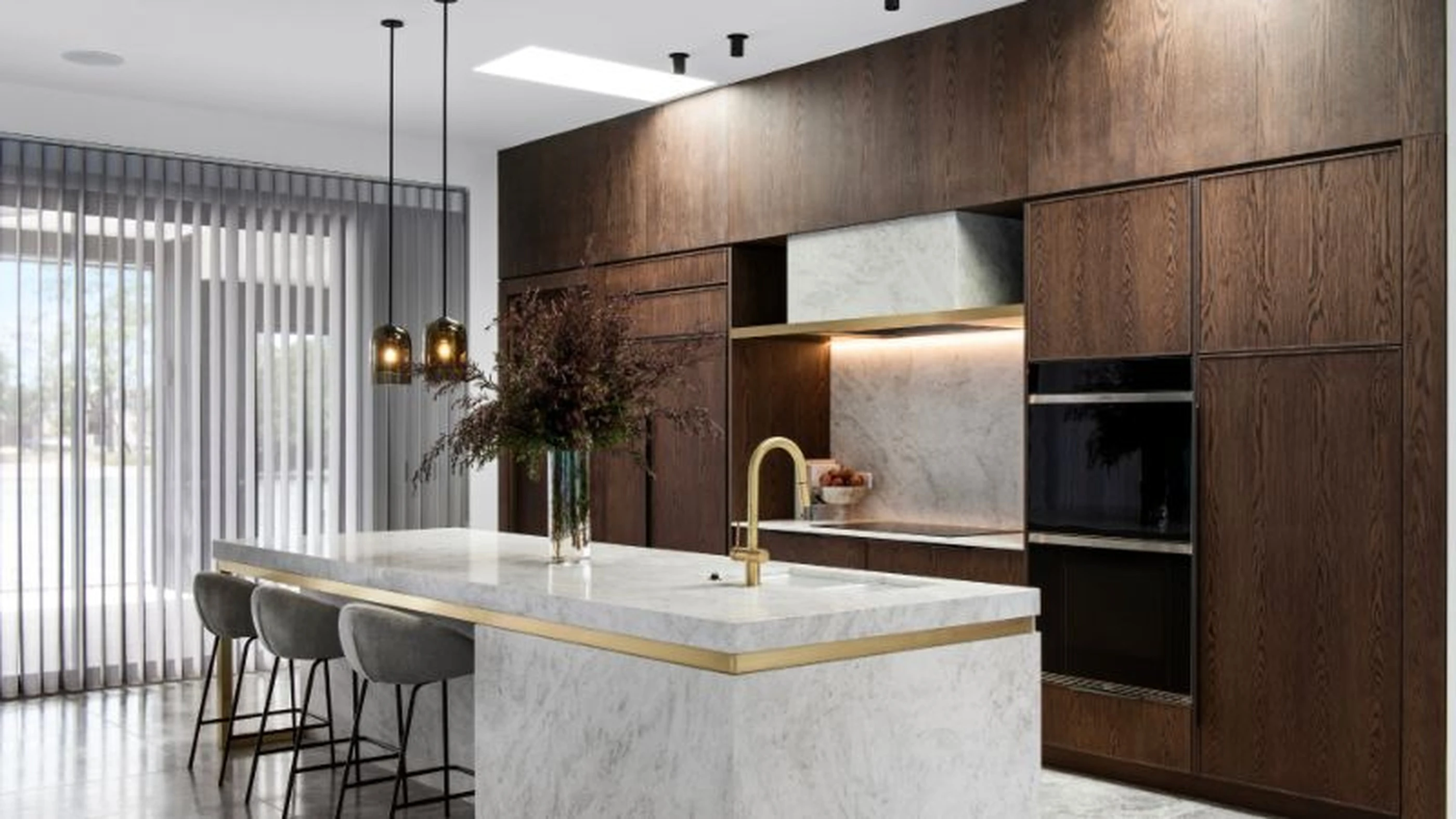 Modern kitchen with dark wood cabinets, white marble island with gold trim, gray barstools, and pendant lighting.