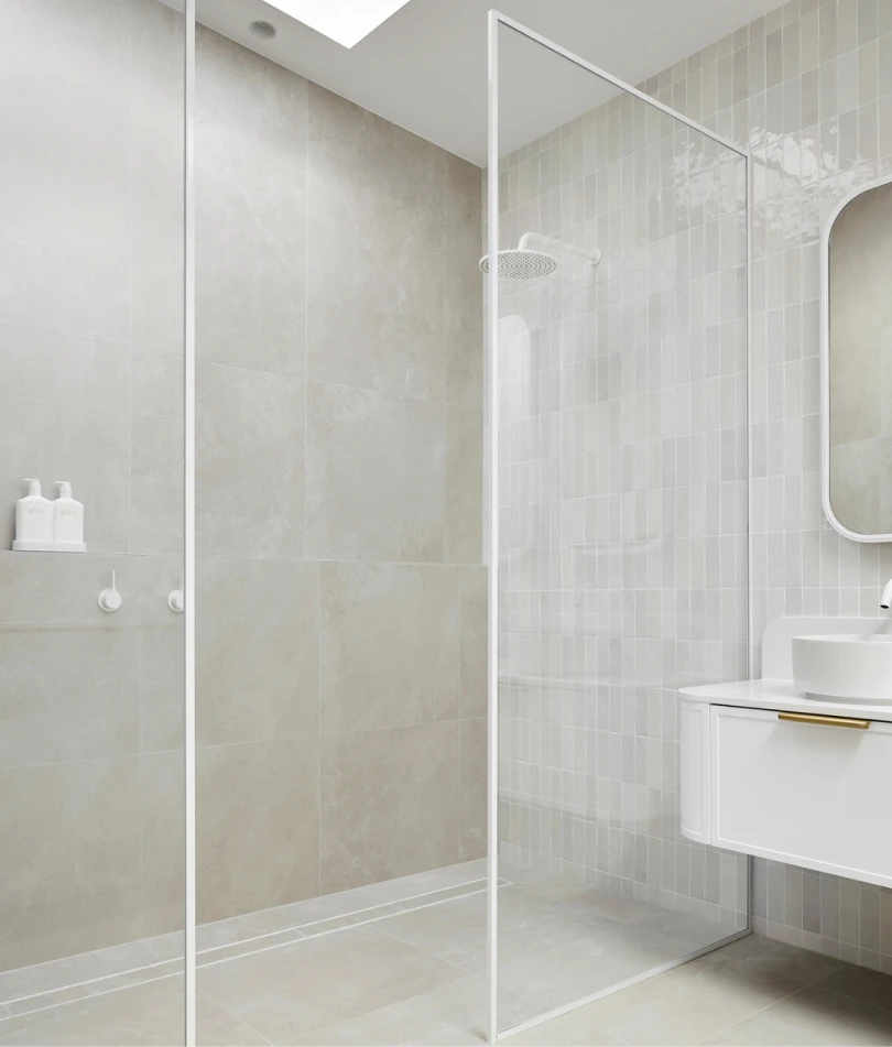 Modern bathroom with glass shower enclosure, light beige tiles, white sink cabinet, and skylight.