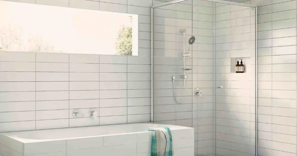 Modern white bathroom with bathtub, glass shower enclosure, window, and turquoise towel draped over tub edge.