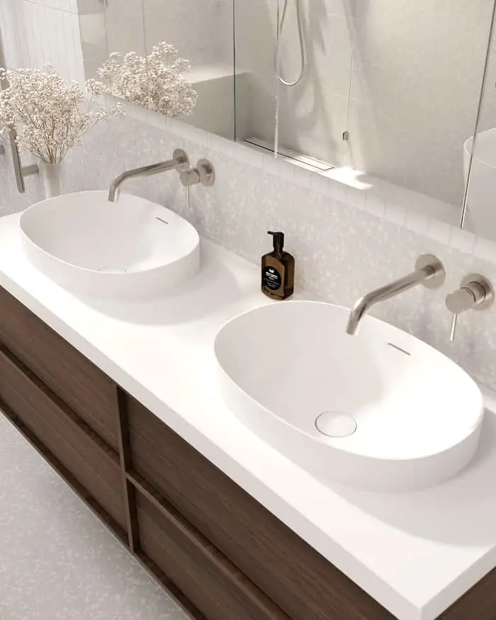 Modern bathroom with double white oval sinks on dark wood vanity, wall-mounted faucets, and dried flowers in a vase.