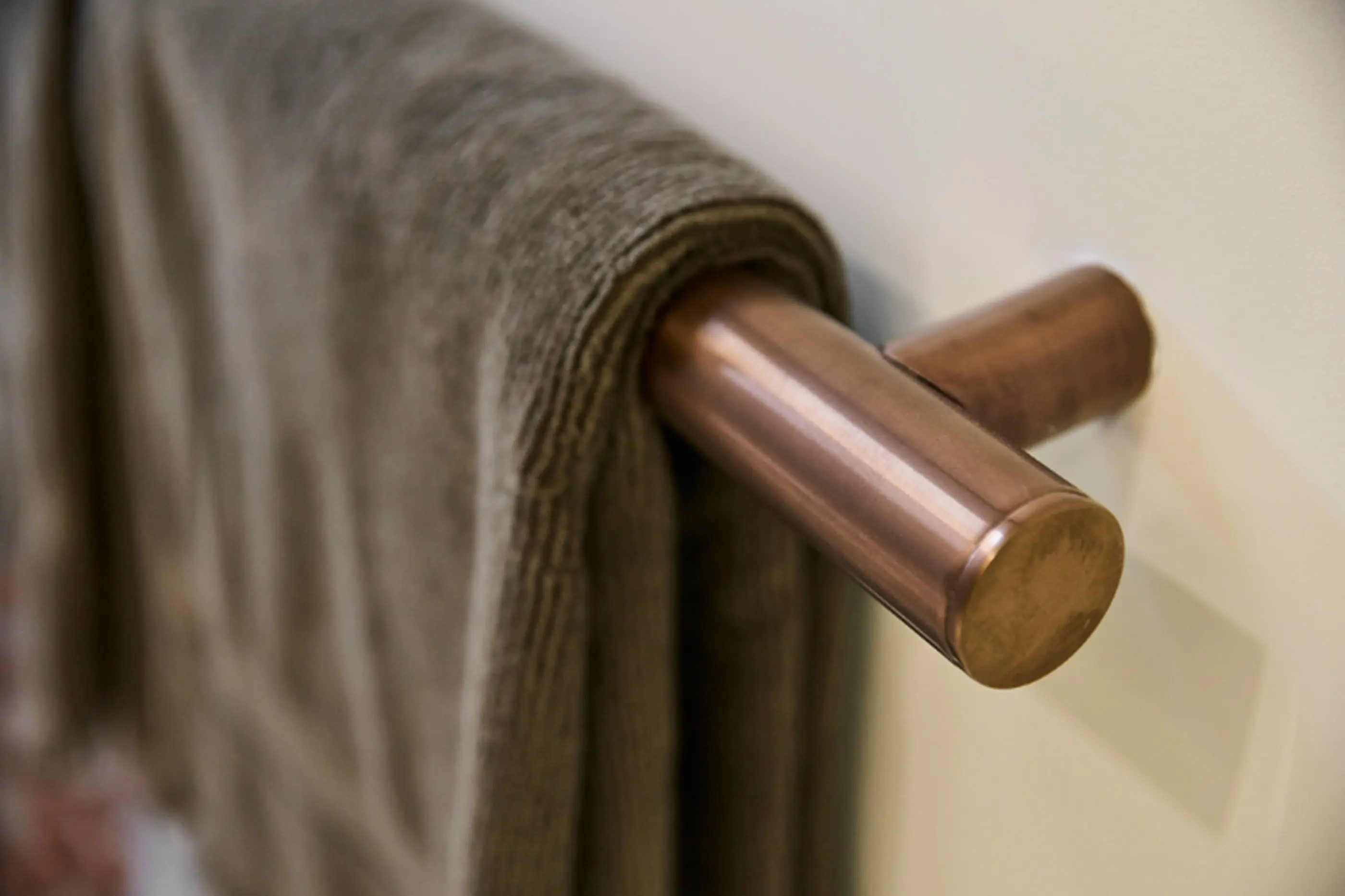 Gray towel hanging on a copper towel bar mounted on a light-colored wall.