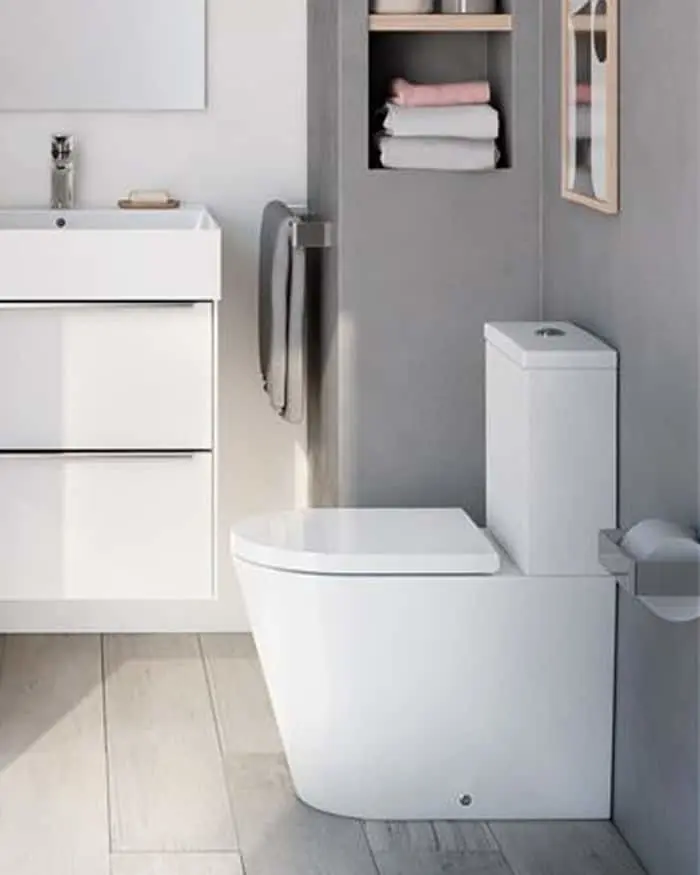 Modern bathroom with white toilet, sink cabinet, and built-in gray shelf containing folded towels.